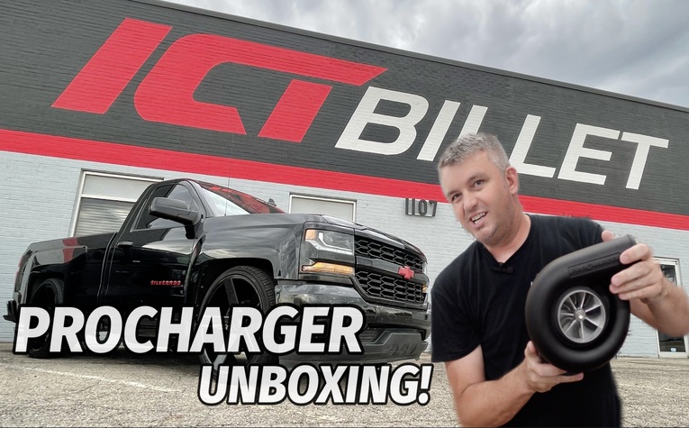 ICT Billet’s Brandon holds a supercharger in front of their short wide truck parked in front of the ICT Billet Building.